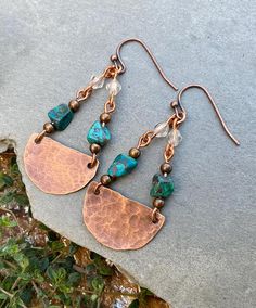 two copper and turquoise stone dangle earrings on top of a gray rock with grass in the background