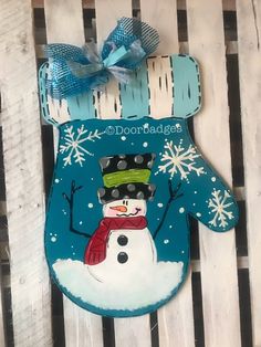 a snowman mitt ornament hanging on a wooden fence with blue ribbon