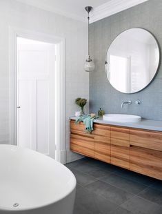 a white bath tub sitting next to a bathroom sink under a round mirror on a wall