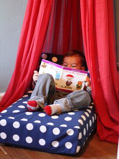 a small child reading a book in a bed with red curtains and polka dots on it