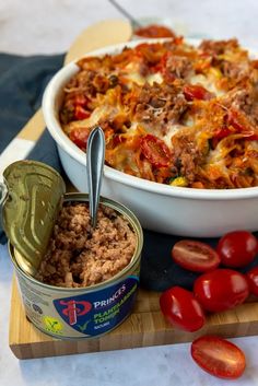 a casserole dish with meat and tomatoes next to it on a cutting board