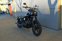 a black motorcycle parked in front of a building with a shadow on the wall behind it