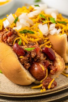 two chili dogs with cheese and onions on a plate