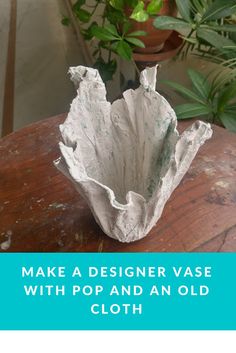 a white vase sitting on top of a wooden table next to a potted plant