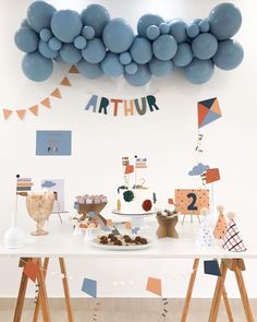 a table topped with lots of blue balloons and desserts on top of wooden tables