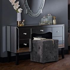 a mirror on the wall above a desk with a stool and flowers in front of it