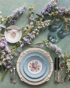 the table is set with plates, silverware and purple flowers on top of it