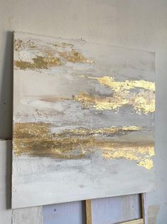 a painting with gold paint on it in a white frame next to a wall mounted easel