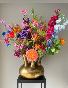 a vase filled with lots of colorful flowers on top of a black table next to a white wall