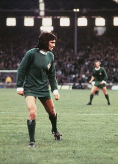 two men playing soccer on a field with fans in the stands watching from behind them