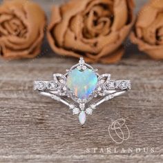 a white opal and diamond ring with roses in the background on a wooden table