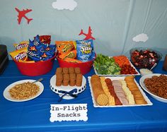 a blue table topped with plates and bowls filled with food next to a sign that says in flight snacks