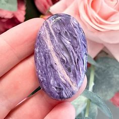 a person holding a purple stone in their hand next to pink roses and other flowers