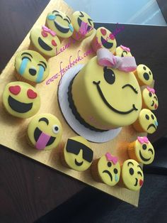 there is a yellow cake with many smiley faces on it and some cupcakes