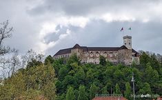 a castle on top of a hill with trees around it and clouds in the sky