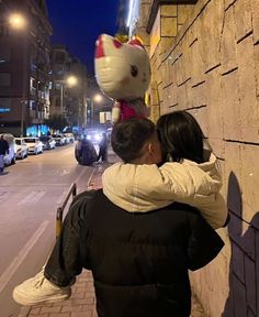 a man and woman hugging on the side of a building with a hello kitty balloon attached to their back