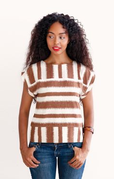 a woman wearing a brown and white striped sweater with her hands in her pockets while standing against a wall