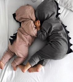 a baby sleeping on top of a bed wearing a dinosaur costume with his head turned to the side