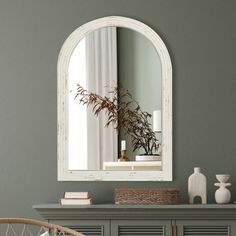 a mirror is hanging on the wall above a dresser with a basket and vases