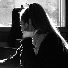 a woman sitting in front of a window talking on a cell phone while holding her hand to her face