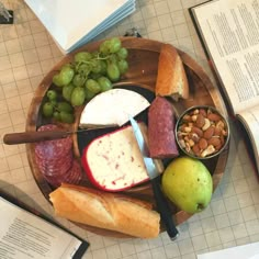 a wooden plate topped with meat, cheese and fruit next to an open book on top of a table