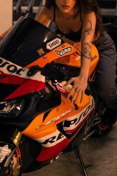 a woman sitting on top of an orange and black motorbike in a garage