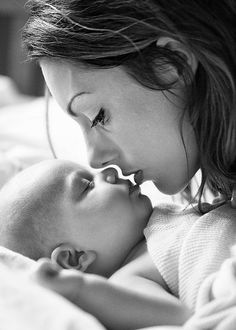 a woman is kissing her baby on the cheek while laying in bed with it's eyes closed