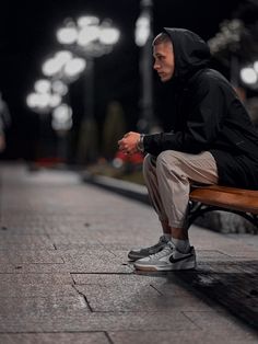 a man sitting on top of a wooden bench next to a street light at night