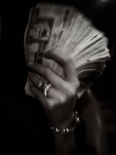 a woman holding up a bunch of money in her hand at night time with the light on