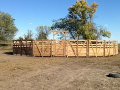 a large wooden structure sitting in the middle of a dirt field next to some trees