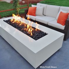 a fire pit sitting on top of a patio next to a white couch and orange pillows