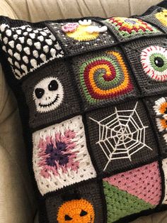 a crocheted pillow with halloween decorations on it sitting on a couch next to a white chair