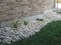 some rocks and grass near a brick wall with a window in the corner that is next to it