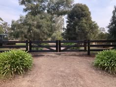 a gated in area with trees and bushes surrounding it on a dirt road that leads to a grassy field