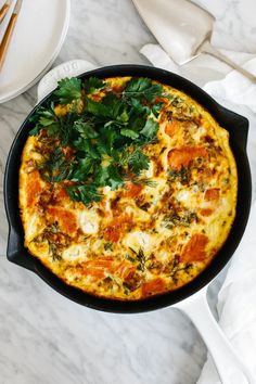 an omelet with tomatoes and parsley in a cast iron skillet on a marble table