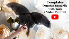 a woman holding a black butterfly in front of white flowers with the words templates organza butterfly with tails and video tutor