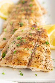 two fish fillets on a white plate with lemons and parsley garnish