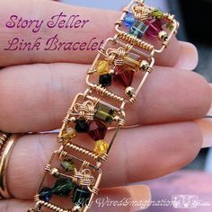 a hand holding a gold bracelet with multicolored stones on it's sides