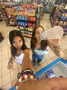 two girls standing in front of a store counter drinking from a water bottle and looking up at the camera