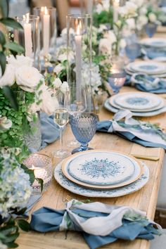 the table is set with blue and white plates, napkins, candles and flowers