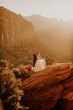 a bride and groom standing on top of a rock in the mountains at sunset,