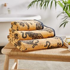 three towels are stacked on top of a stool in front of a bathtub and potted plant