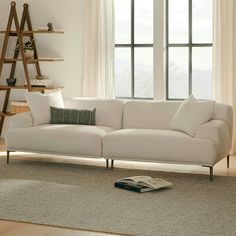 a white couch sitting in front of a window next to a book shelf on top of a rug