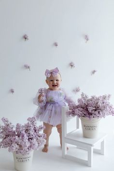 a baby girl standing next to some flowers