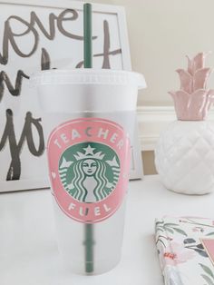 a starbucks cup sitting on top of a white table next to a pink flower vase