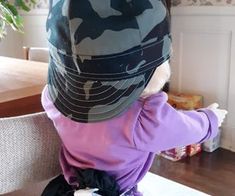 a little boy sitting at a table with a hat on top of his head and wearing a purple shirt