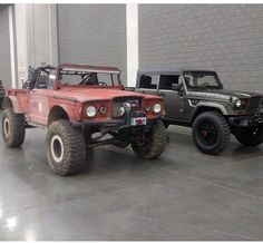 two jeeps parked next to each other in front of a garage door with large tires on them