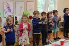 a group of young children standing next to each other in front of a wall with pictures on it