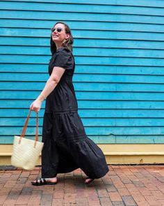 a woman is walking down the street carrying a straw bag and wearing black dress with heels