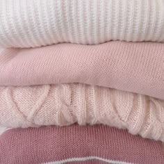 four sweaters stacked on top of each other in pink and white colors, all folded neatly